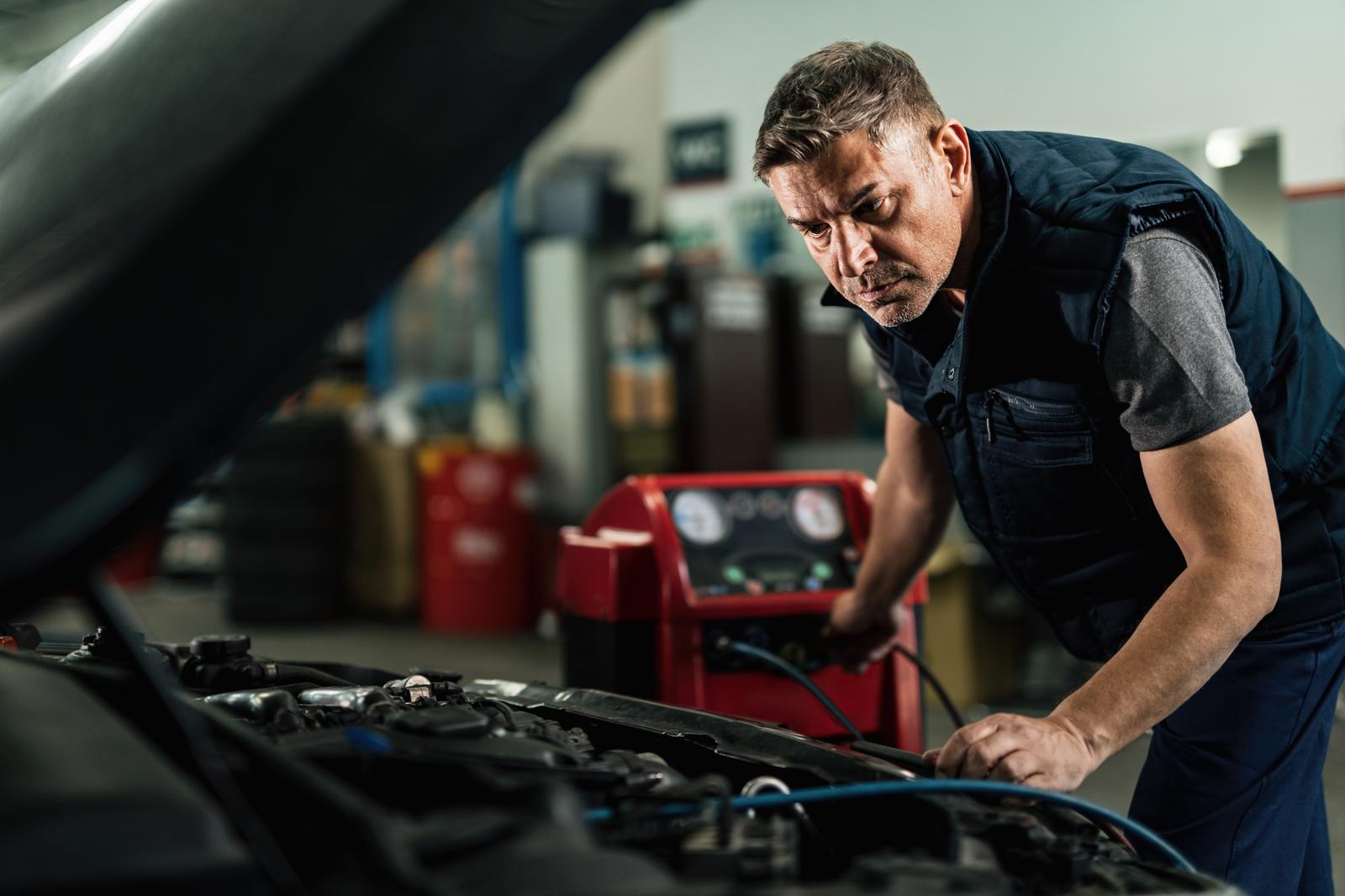 Technician servicing a car's air conditioning system with a refrigerant machine in the background