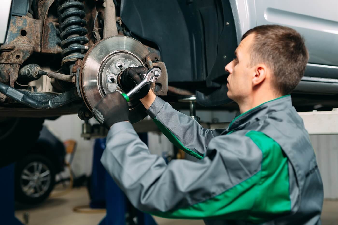 Technician servicing a brake rotor and caliper on a raised vehicle