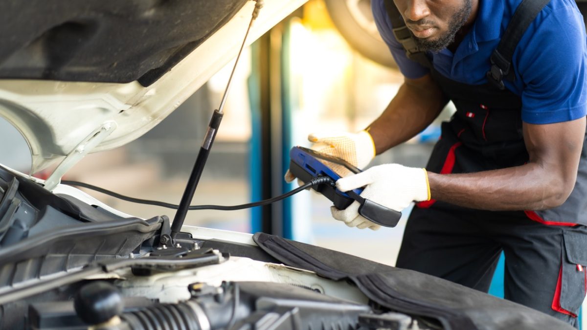 Technician holding a diagnostic scanner plugged into a car with its hood open
