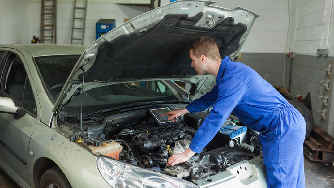 Technician reviewing diagnostic readings on a tablet at the front of a car with its hood raised